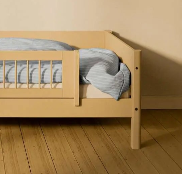 FLEXA SAND short safety rail from WHITE & NOR on toddler bed with blue-striped bedding in a beige childrenβs room.